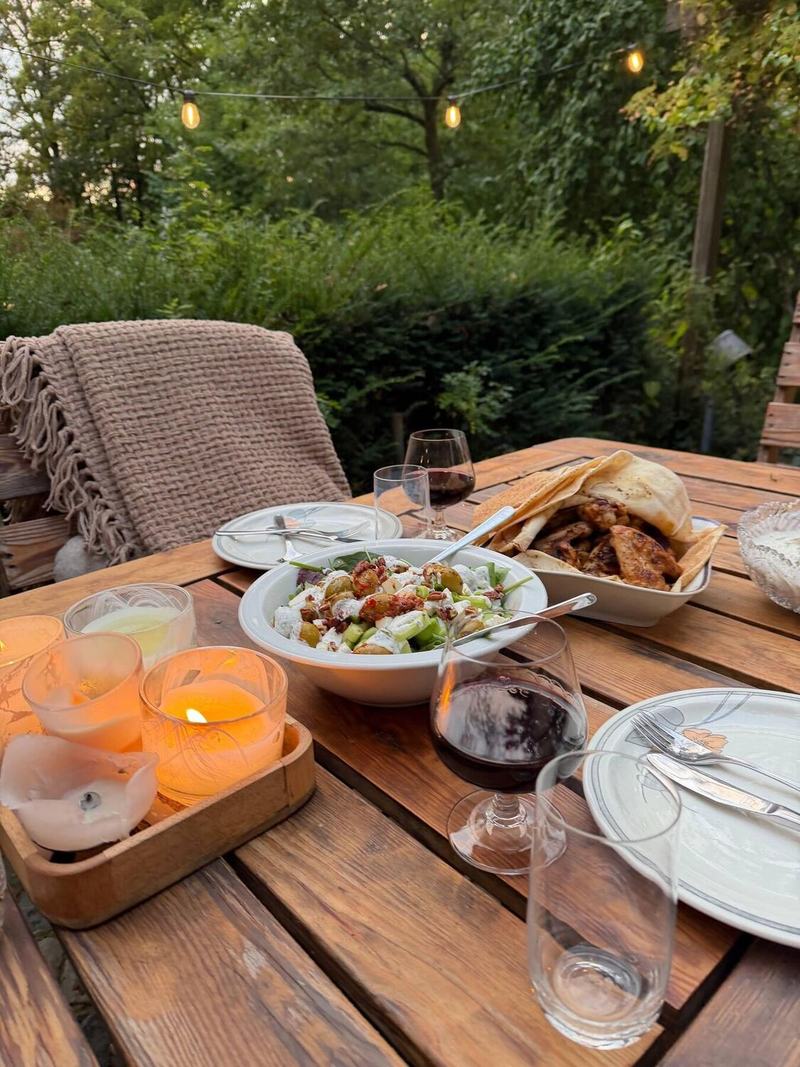 Gedeckter Holztisch am Abend mit Salat, Rotwein und Windlichtern unter Lichterketten