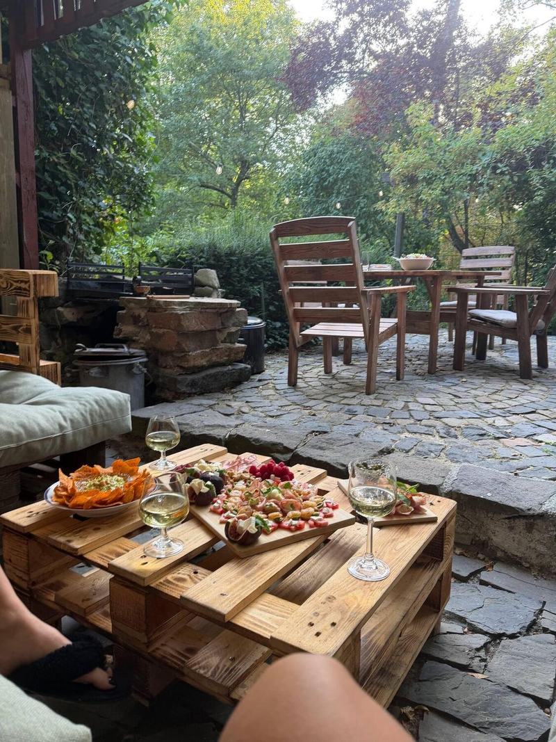 Wein und Snacks auf dem Palettentisch, dahinter der Grill aus Naturstein und Gartenstühle