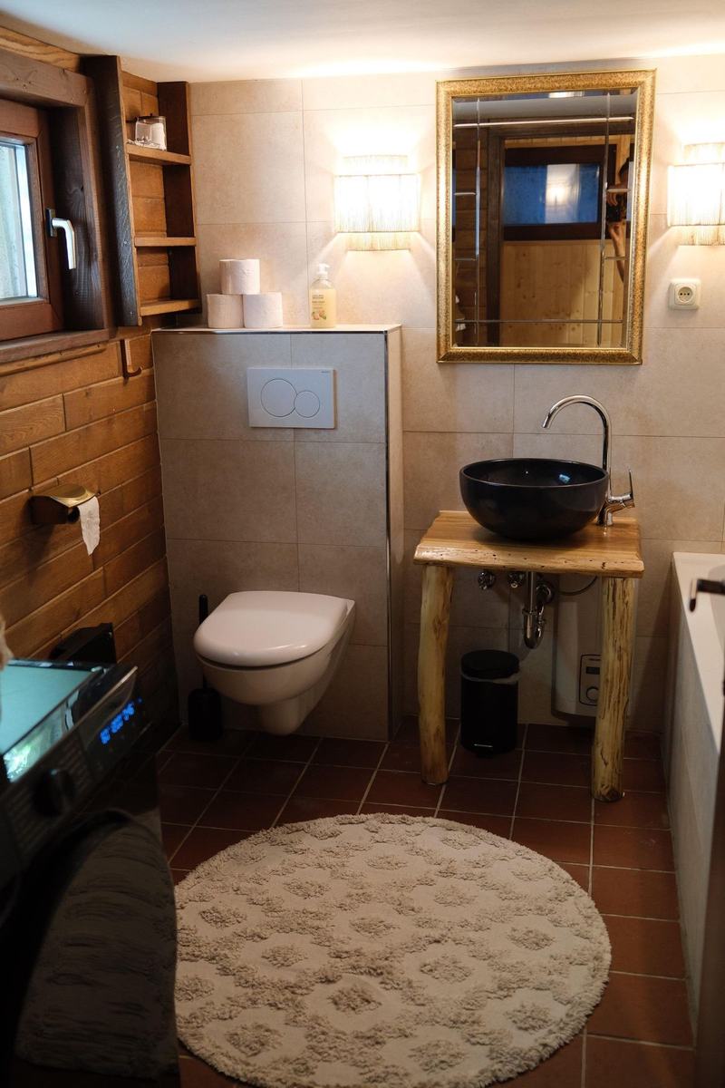 Badezimmer mit Waschschale auf Holzgestell, goldgerahmtem Spiegel und rundem Teppich