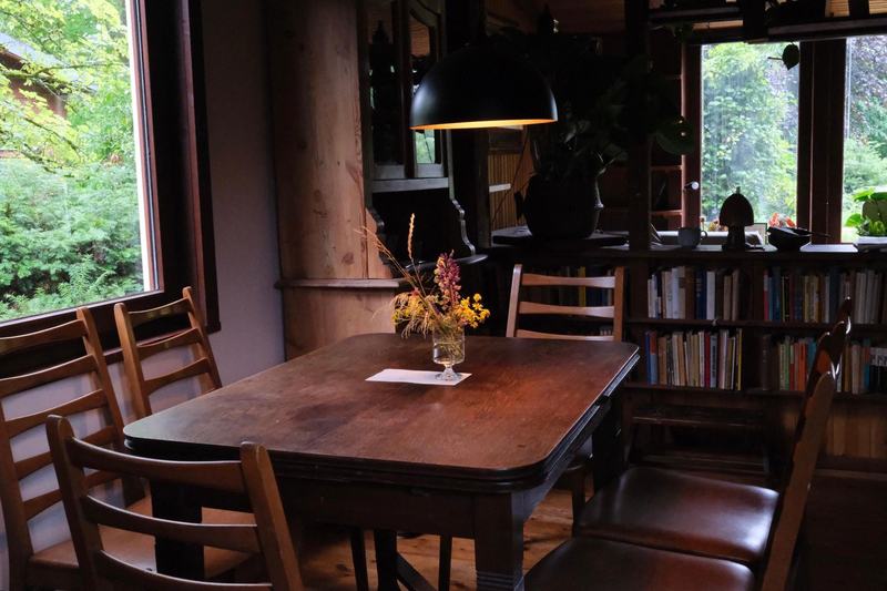 Holzesstisch mit Wiesenblumen vor einer Bücherwand und Fenstern ins Grüne