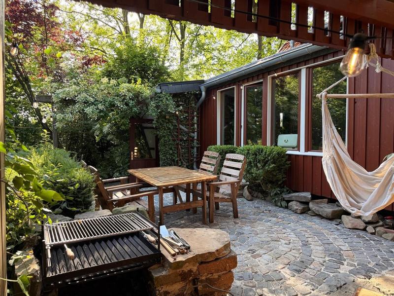Terrasse aus Kopfsteinpflaster mit Grill, Holztisch und Hängematte an der roten Hauswand