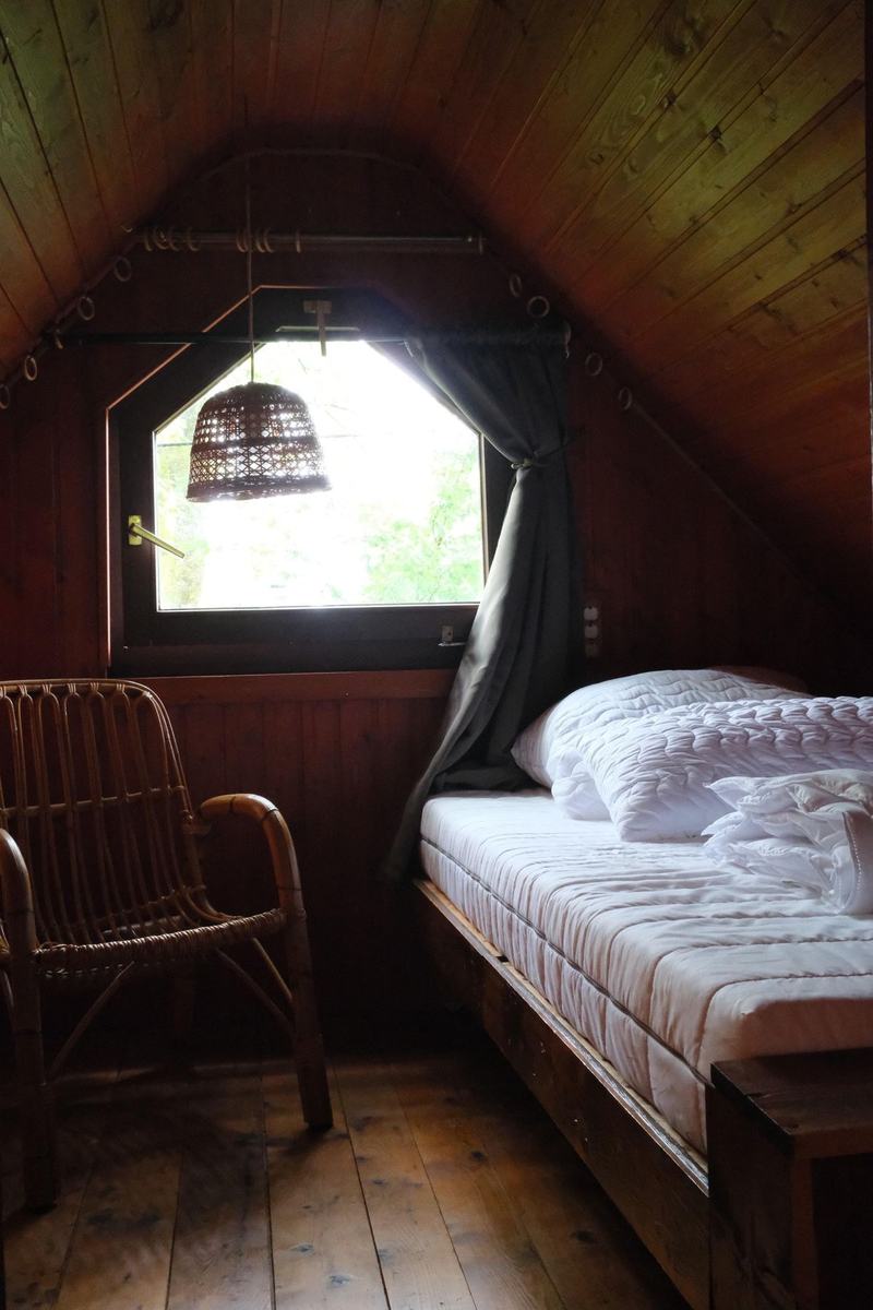 Zimmer 1: Doppelbett mit Korbsessel unter dem Giebelfenster, ringsum Holzverkleidung